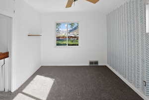 Spare room featuring dark colored carpet and a ceiling fan