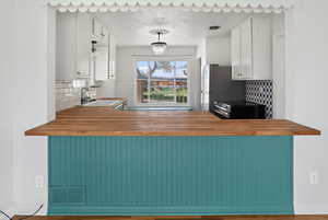Kitchen with wooden counters, white cabinetry, stainless steel appliances, backsplash, and a textured ceiling