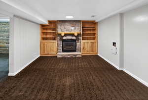 Unfurnished living room with dark colored carpet, a stone fireplace, and built in shelves