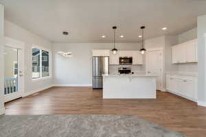 Kitchen featuring stainless steel appliances, white cabinetry, light wood-style flooring, and decorative light fixtures