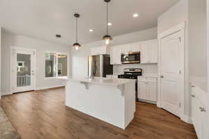 Kitchen featuring stainless steel appliances, white cabinetry, a kitchen bar, and dark wood-type flooring