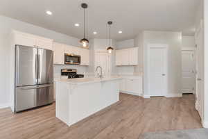 Kitchen with stainless steel appliances, white cabinets, a kitchen breakfast bar, and decorative light fixtures