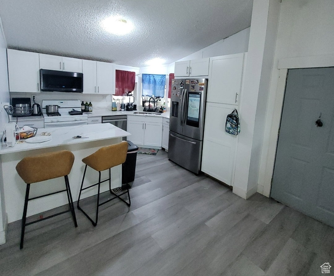Kitchen with a breakfast bar, a textured ceiling, stainless steel appliances, a peninsula, and white cabinetry