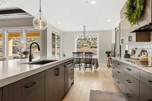 Kitchen with decorative light fixtures, light wood finished floors, exhaust hood, dark wood finish cabinets, and modern cabinets