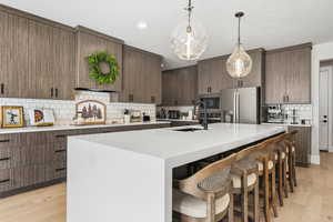 Kitchen featuring a kitchen island with sink, light wood-style floors, a kitchen breakfast bar, stainless steel fridge with ice dispenser, and hanging light fixtures