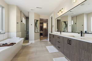 Full bathroom featuring double vanity, a walk in closet, a stall shower, a soaking tub, and light tile patterned floors