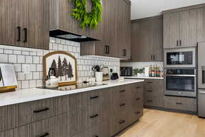 Kitchen with black appliances, light wood-type flooring, tasteful backsplash, and dark wood finish cabinets