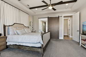Bedroom featuring carpet flooring, a barn door, a tray ceiling, a ceiling fan, and recessed lighting
