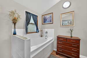 Bathroom featuring a bath, vaulted ceiling, vanity, and dark wood-style flooring