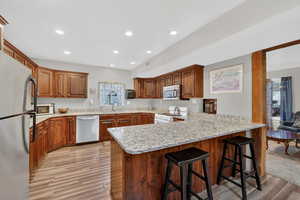 Kitchen featuring a breakfast bar area, a peninsula, stainless steel appliances, light wood-type flooring, and recessed lighting