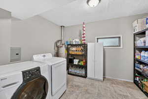 Laundry room featuring a textured ceiling, washing machine and clothes dryer, electric panel, and water heater