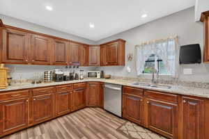 Kitchen featuring stainless steel dishwasher, light stone counters, light wood-type flooring, white microwave, and wood finish cabinets