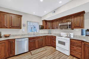 Kitchen with stainless steel appliances, light stone countertops, and light wood-style flooring