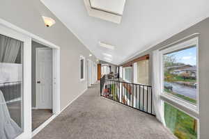 Hall with vaulted ceiling, light carpet, healthy amount of natural light, and ornamental molding