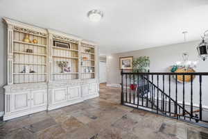 Corridor with hanging lights, an upstairs landing, and stone tile flooring