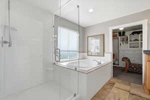 Primary Suite Bathroom featuring a spacious closet, a stall shower, a bath, stone finish flooring