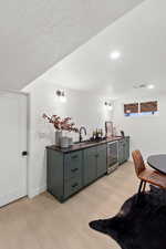 Indoor wet bar with dark countertops, a textured ceiling, light wood-style flooring, green cabinetry, and wine cooler