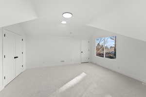 Bonus room with lofted ceiling and light colored carpet
