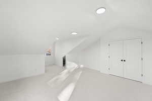 Bonus room with vaulted ceiling and light colored carpet