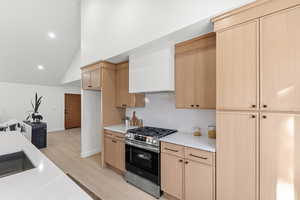 Kitchen with stainless steel range with gas stovetop, lofted ceiling, light wood finish cabinets, light wood-style floors, and open floor plan