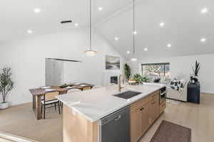 Kitchen with light wood-style flooring, light wood finish cabinets, a center island with sink, open floor plan, and a high ceiling