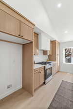 Kitchen featuring stainless steel range with gas stovetop, light wood-type flooring, light wood finish cabinets, light countertops, and decorative backsplash