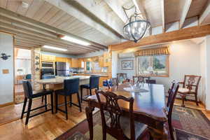 Dining space with light wood-type flooring, suspended lighting, a wooden ceiling with exposed beams, and a baseboard heating unit
