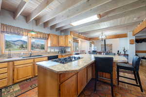 Kitchen featuring a wood ceiling with exposed beams, a wood stove, hanging lights, wood finish cabinetry, and a kitchen breakfast bar