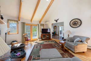 Living area featuring vaulted ceiling, light wood-style floors, and a baseboard heating unit