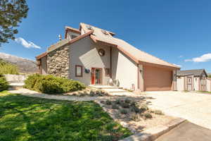 View of front of house featuring concrete driveway, a metal roof, an attached garage, stone siding, and a front yard