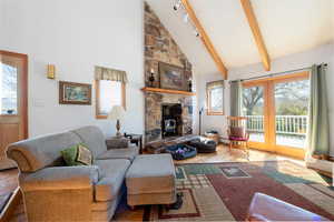 Living room featuring vaulted ceiling, a wood stove, light wood-type flooring, and rail lighting