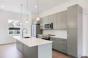 Kitchen featuring gray cabinetry, stainless steel appliances, backsplash, and an island with sink
