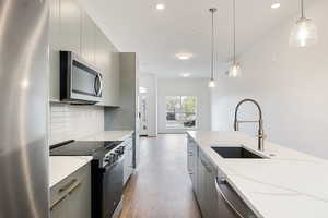 Kitchen with stainless steel appliances, light wood-style flooring, hanging light fixtures, modern cabinets, and gray cabinetry