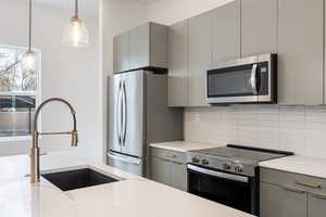 Kitchen with gray cabinetry, stainless steel appliances, modern cabinets, and hanging light fixtures