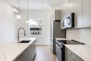 Kitchen with stainless steel appliances, gray cabinets, hanging light fixtures, and light wood-style floors