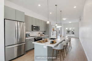 Kitchen with stainless steel appliances, a kitchen breakfast bar, gray cabinetry, light wood-type flooring, and a center island with sink