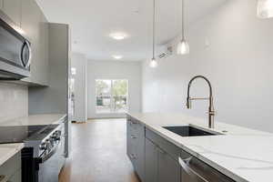 Kitchen featuring gray cabinets, stainless steel appliances, light stone counters, backsplash, and pendant lighting