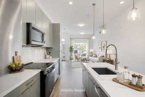 Kitchen with electric range, stainless steel microwave, open floor plan, gray cabinetry, and decorative light fixtures