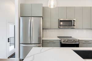 Kitchen with stainless steel appliances, gray cabinets, light stone counters, and tasteful backsplash