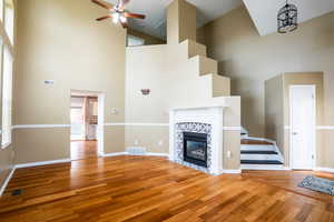 Unfurnished living room with a tile fireplace, wood finished floors, a high ceiling, and a ceiling fan
