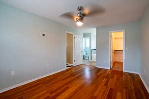 Unfurnished bedroom featuring a spacious closet, hardwood / wood-style floors, a ceiling fan, and ensuite bath