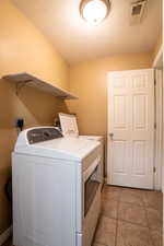 Laundry room with a textured ceiling, light tile patterned floors, and washing machine and clothes dryer