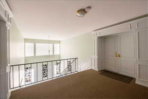 Hallway featuring a decorative wall, dark carpet, and hanging lights