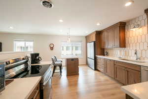 Kitchen featuring stainless steel appliances, wood finish cabinets, light wood-style flooring, tasteful backsplash, and plenty of natural light