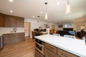Kitchen featuring open floor plan, stainless steel appliances, light wood-type flooring, light stone countertops, and pendant lighting