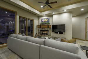 Living room with stone tile flooring, a ceiling fan, recessed lighting, an outdoor stone fireplace, and a tray ceiling