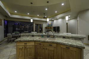 Kitchen with a raised ceiling, ceiling fan, open floor plan, wood finish cabinets, and decorative light fixtures