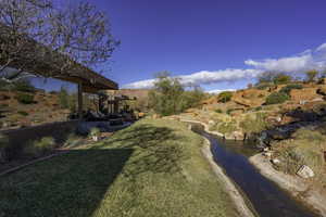 View of grassy yard featuring a garden pond and a patio