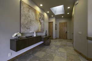 Hallway with a skylight, light stone finish floors, and recessed lighting