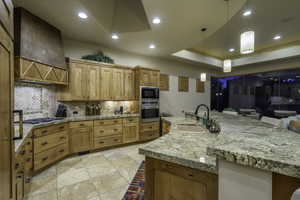Kitchen with a raised ceiling, stainless steel appliances, light stone countertops, decorative light fixtures, and a breakfast bar